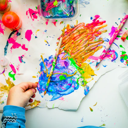 Mano de un niño pintando con un pincel sobre un papel lleno de colores