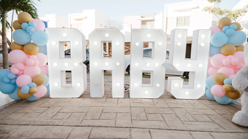 Letras luminosas que forman «baby» entre dos columnas de globos, en una fiesta