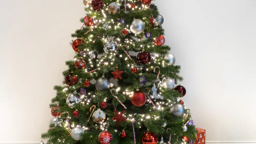 Árbol de Navidad con luces y bolas rojas y plateadas, junto a una pared clara